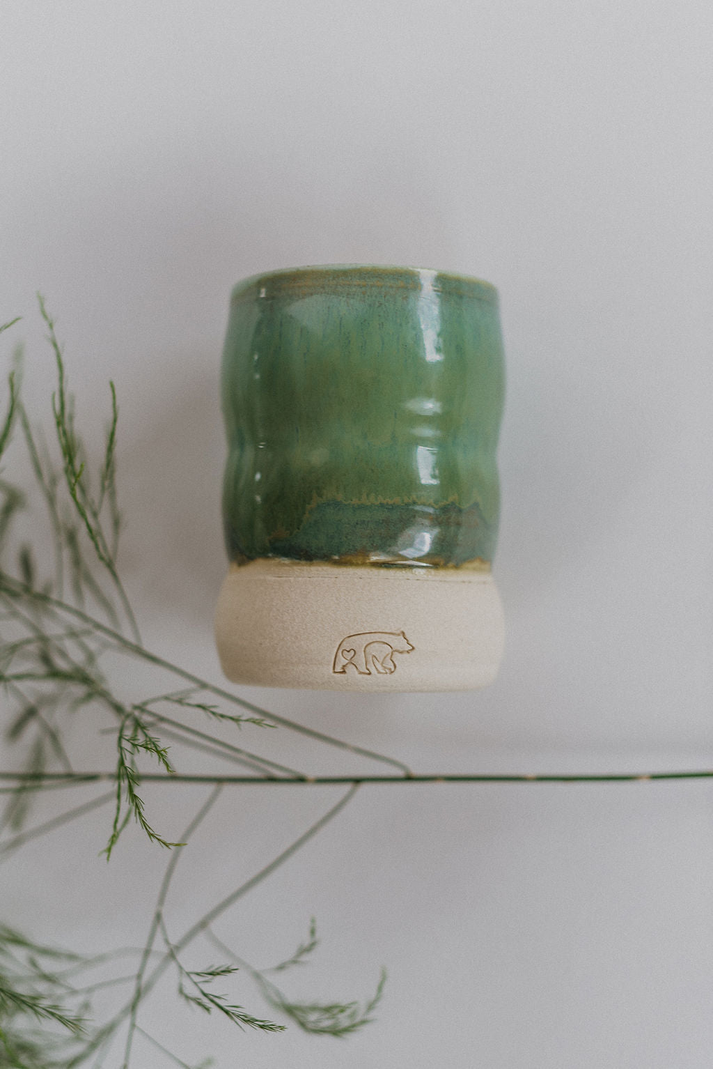 A green ceramic candle vessel with the wick and bear logo.