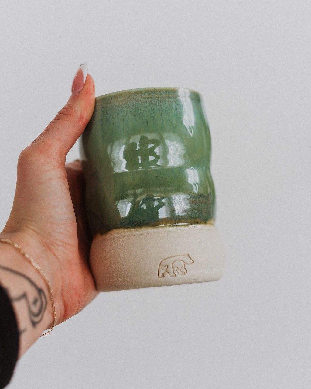 A hand holding a green ceramic candle vessel.