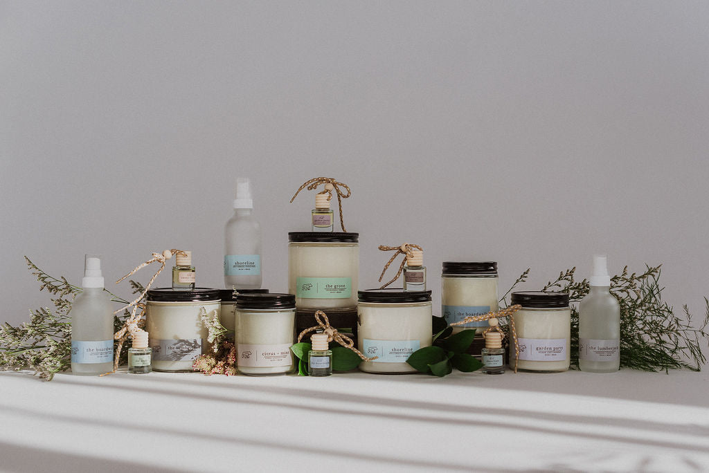 A range of diffusers, sprays, and scented candle products arranged aesthetically with sprigs of greenery.